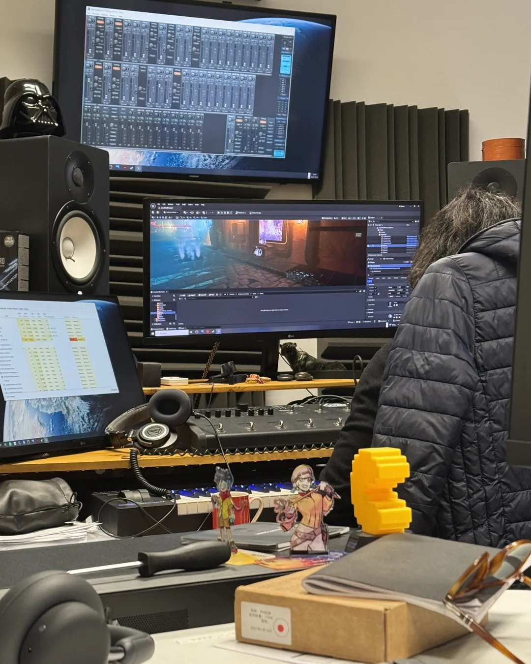 An NC Gaming developer at a studio desk, Ezekiel open in the Unreal editor on one monitor and an audio session on another.